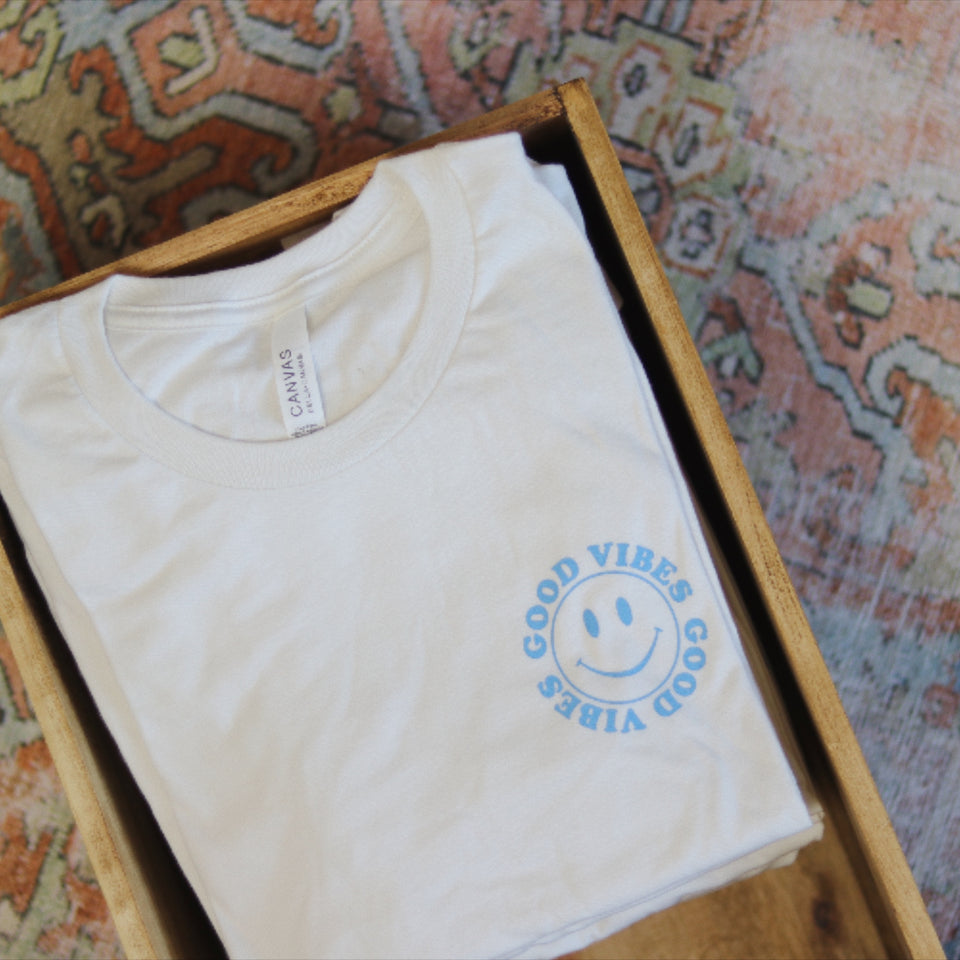 Good Vibes t-shirt in wooden crate on colorful oriental rug.